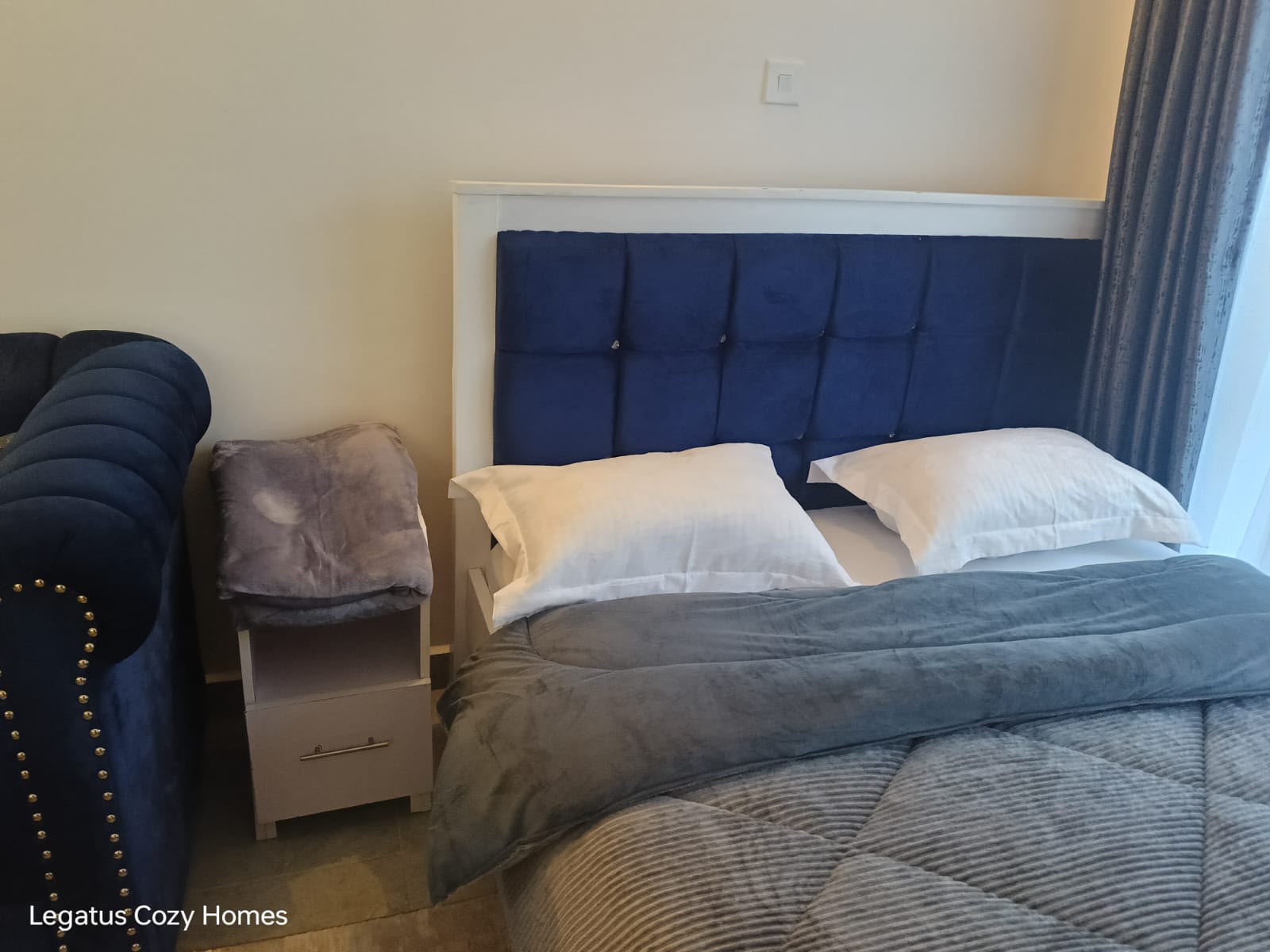 Queen bed with blue tufted headboard and fresh white linen at Tsavo Sentinel