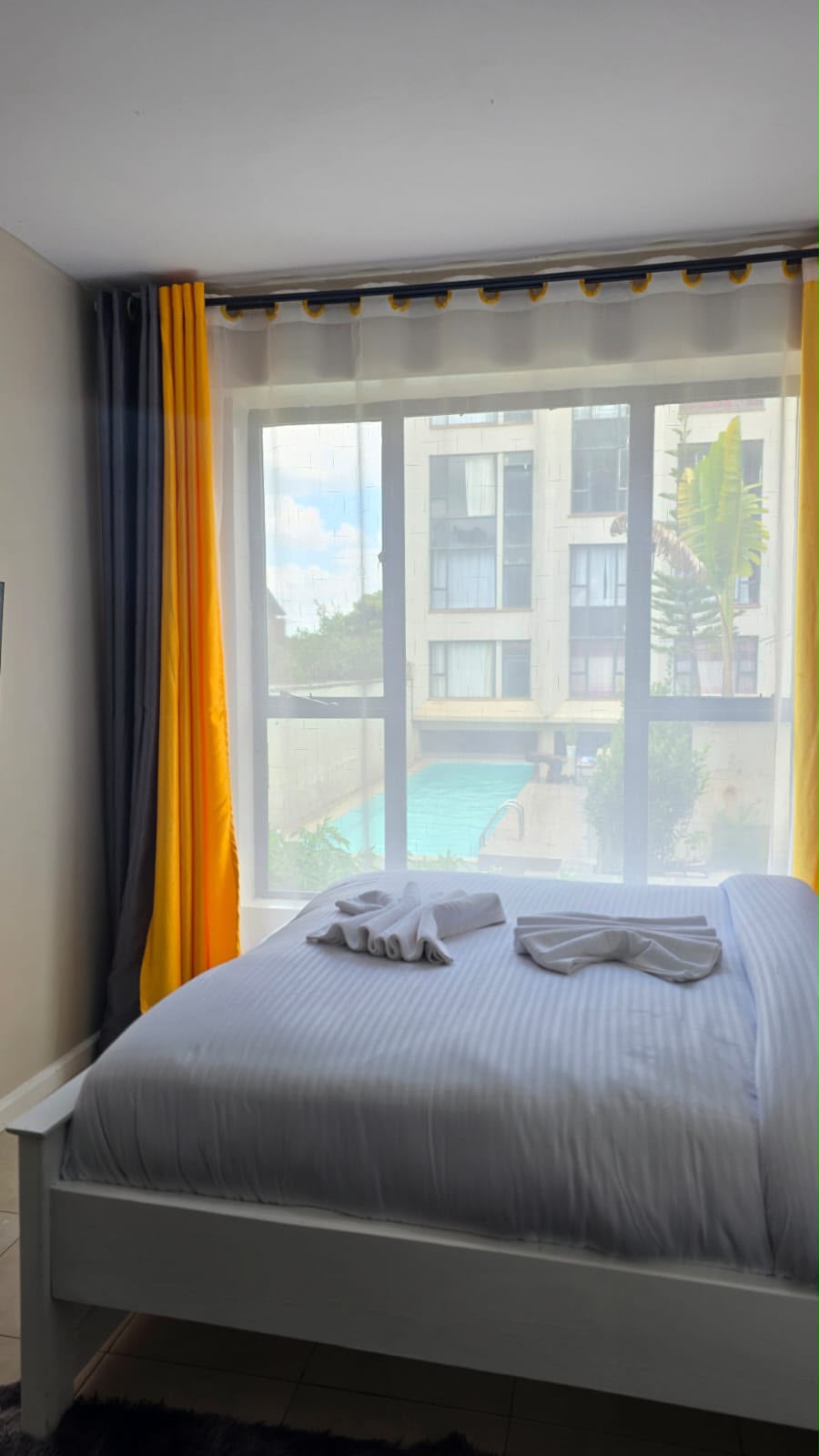 Main bedroom with queen bed, white linen and pool view window in the Tsavo Rongai two bedroom apartment